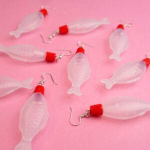 A bunch of different soy sauce earrings are scattered across a pink backdrop. They all point in different directions