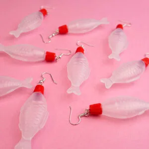 A bunch of different soy sauce earrings are scattered across a pink backdrop. They all point in different directions