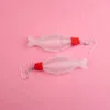 A pair of soy sauce earrings against a pink backdrop