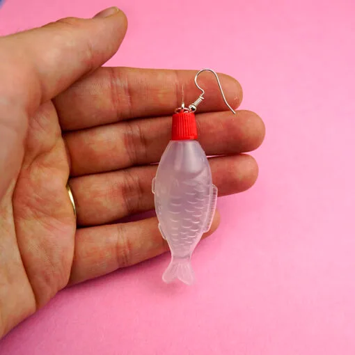Someone holds a single soy sauce earring against a pink backdrop