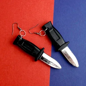 A pair of our knife earrings are placed on a red and blue split surface. They have black handles, and a shiny silver knife surface