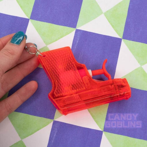 Someone holds a red water pistol earring, against a funky background