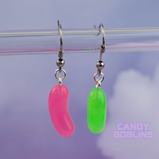 A pair of Jelly bean earrings against a purple cloudy background. They're mismatched and colourful and fun. A Candy Goblins logo is on the bottom.