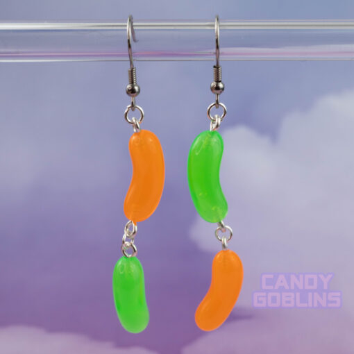 A pair of Jelly bean earrings against a purple cloudy background. They're mismatched and colourful and fun. A Candy Goblins logo is on the bottom.