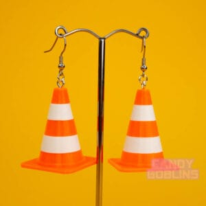 A pair of traffic cone earrings dangle from a silver display. The cones are a bright neon orange, with white stripes.