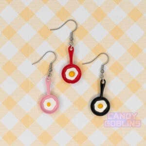 Our egg pan earrings are displayed together. The pans are red, black, and pink, and all have an egg frying on the surface.