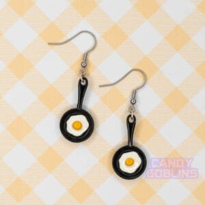 A pair of black egg pan earrings with an egg frying on them.