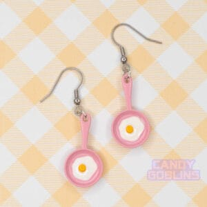 A pair of pink egg pan earrings with an egg frying on them.