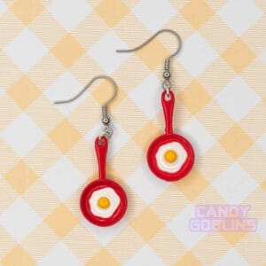 A pair of red egg pan earrings with an egg frying on them.
