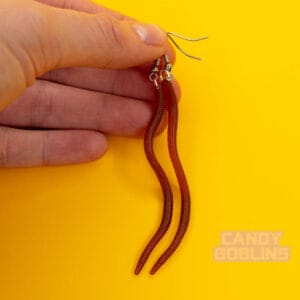 Someone holds a pair of worm earrings. The worms are brown, and look creepily like real earth worms.