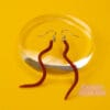 A pair of brown wiggly worm earrings lie against a photo prop. The background is yellow.
