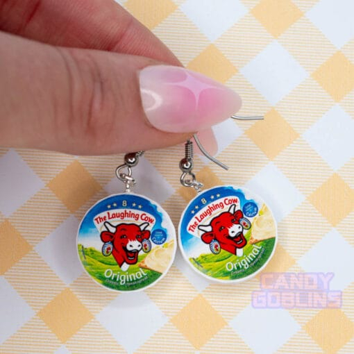 Someone holds a pair of Laughing Cow earrings, they have a decorative pink nail