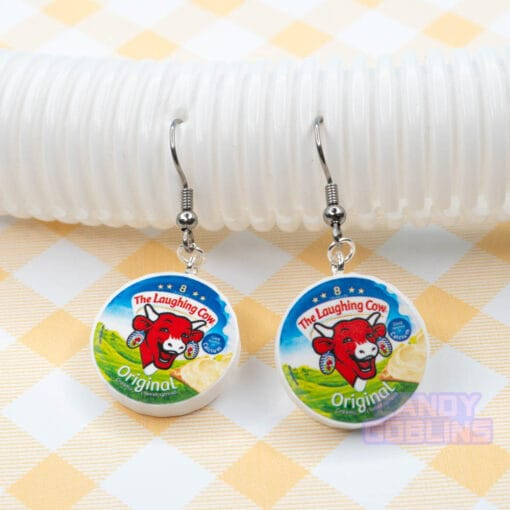 A pair of Laughing Cow earrings lie against a white photo prop