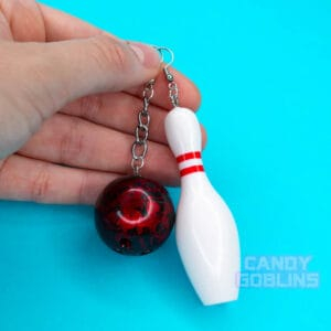 A person holds bowling earrings, one of the earrings is a bowling pin, and the bother a red bowling ball
