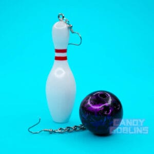 A pair of bowling earrings on a blue background. One earring is a pin, the other a purple ball