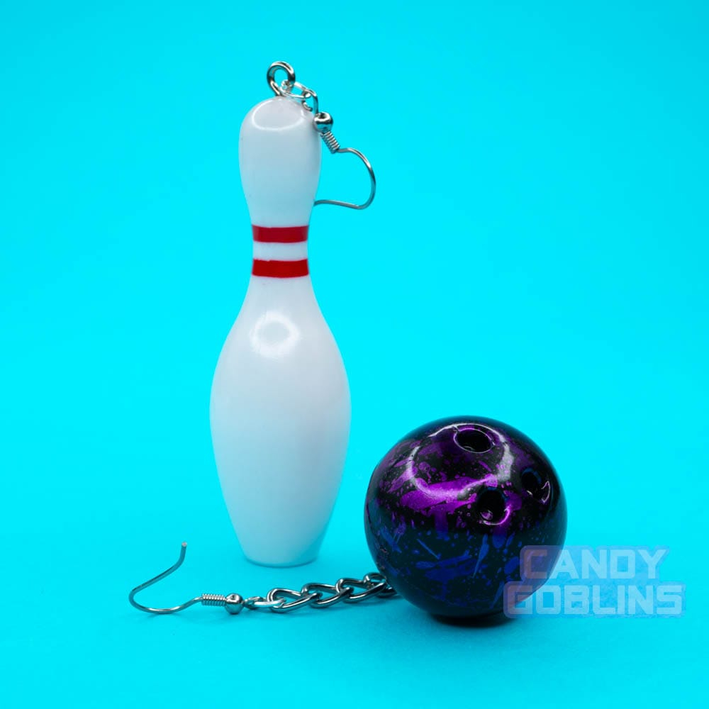 A pair of bowling earrings on a blue background. One earring is a pin, the other a purple ball