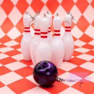 Several bowling pin earrings are lined up with a bowling ball earring that looks ready to hit them