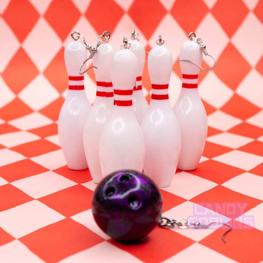 Several bowling pin earrings are lined up with a bowling ball earring that looks ready to hit them