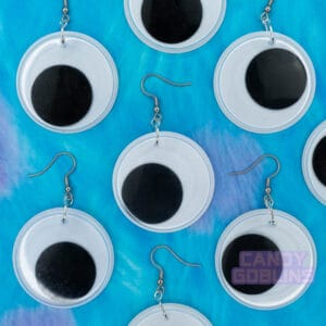Multiple googly eye earrings are laid out against a furry backdrop.