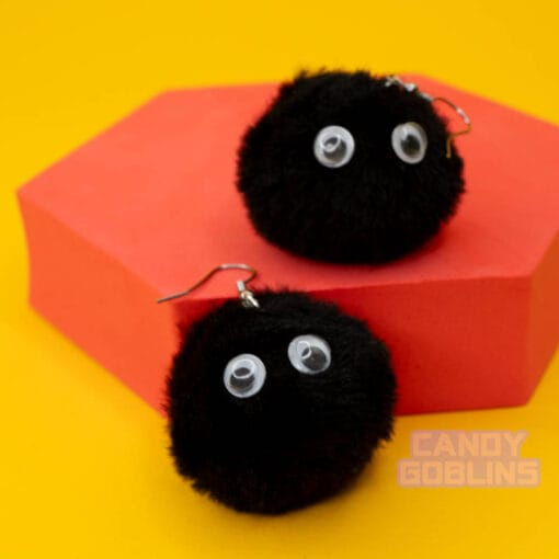 Soot sprite earrings balance on a red photo prop