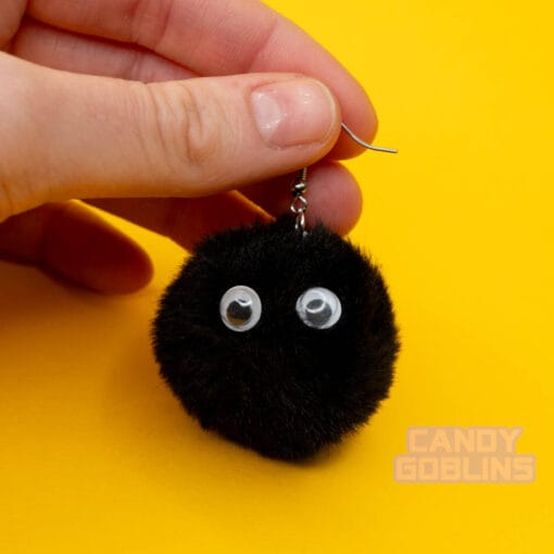 A hand holds our soot sprite earring by the hook