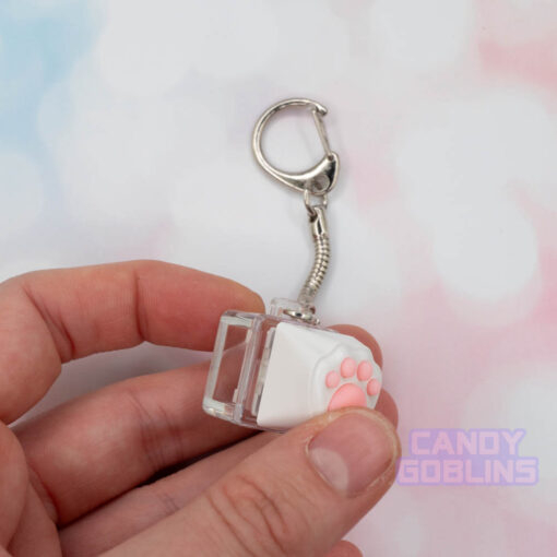 A person pressing a cat keycap keychain featuring a white paw, with pink beans