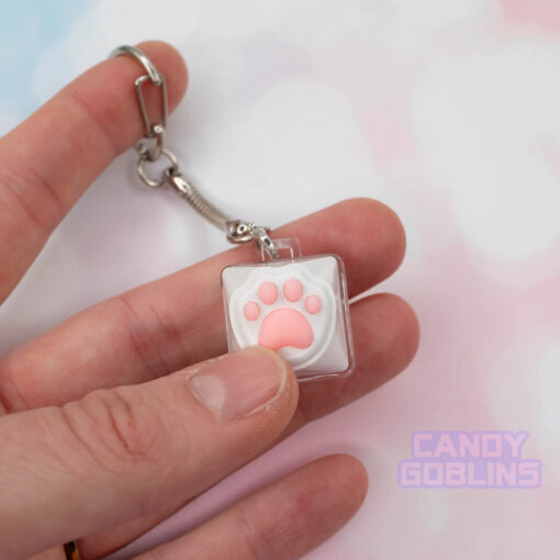 A person pressing a cat keycap keychain featuring a white paw, with pink beans