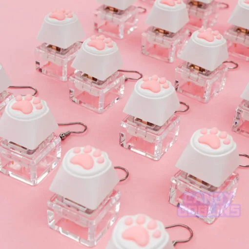Multiple of our Cat Keyboard Switch Earrings are laid out together. The background is a pastel pink.