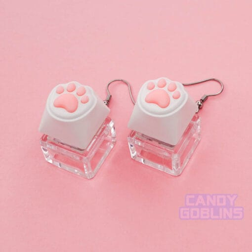 A pair of our Cat Keyboard Switch Earrings shown from the side, this shows off the detail of the pink beans. The background is a pastel pink.