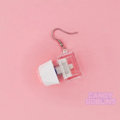 A pair of our Cat Keyboard Switch Earrings shown from the side, this shows off the detail of the pink beans. It also shows the blue keyboard mechanism. The background is a pastel pink.