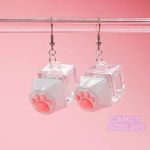 A pair of our Cat Keyboard Switch Earrings hang from a glass display. The background is a pastel pink.