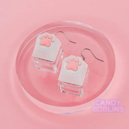 A pair of our Cat Keyboard Switch Earrings posed on a glass photo prop. The background is a pastel pink.