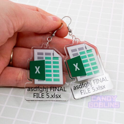 A pair of our Excel Earrings are held against a green backdrop. They feature the Microsoft Excel logo, with text underneath that reads "asdfghj FINAL FILE 5.xlsx"