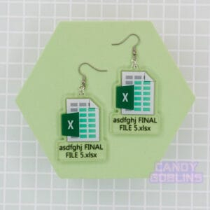 A pair of our Excel Earrings are laid out against a green photo prop. They feature the Microsoft Excel logo, with text underneath that reads 