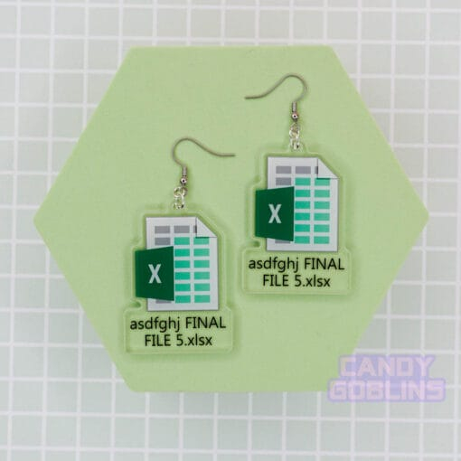 A pair of our Excel Earrings are laid out against a green photo prop. They feature the Microsoft Excel logo, with text underneath that reads "asdfghj FINAL FILE 5.xlsx"