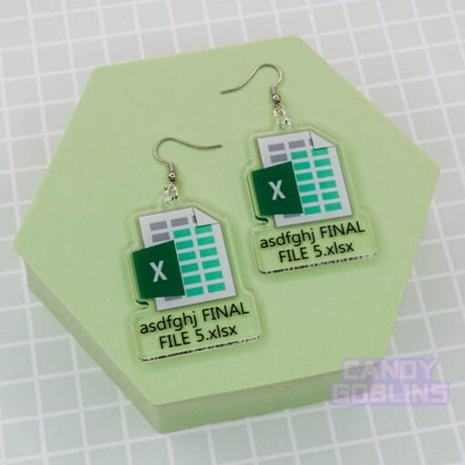 A pair of our Excel Earrings are laid out against a green photo prop. They feature the Microsoft Excel logo, with text underneath that reads "asdfghj FINAL FILE 5.xlsx"