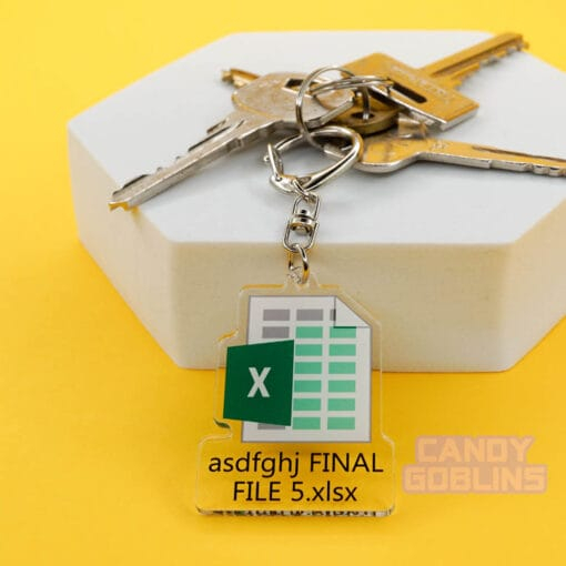 Our Excel Keychain is attached to a pair of keys that are lying on a white photo prop. The background is yellow. The keychain features the Microsoft Excel logo, with text underneath that reads "asdfghj FINAL FILE 5.xlsx"