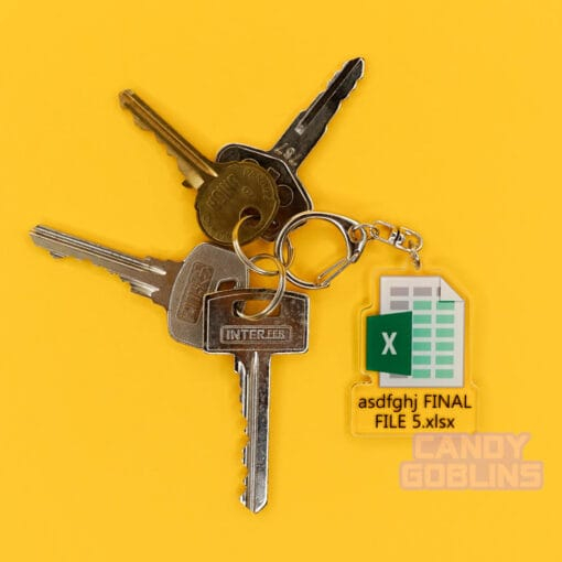 Our Excel Keychain is attached to a pair of keys. They're lying on a yellow background. The keychain features the Microsoft Excel logo, with text underneath that reads "asdfghj FINAL FILE 5.xlsx"