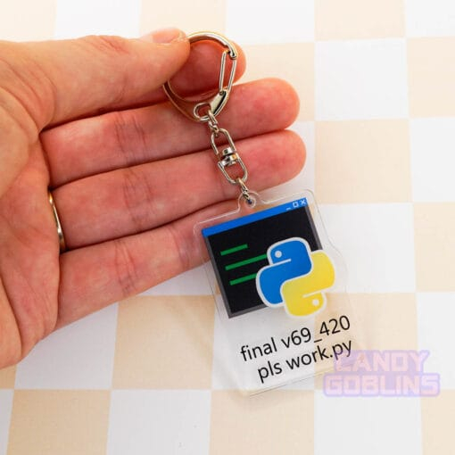 Our Python keychain held against a pastel yellow backdrop. It features the Python logo, with text underneath that reads "final v69_420 pls work.py".