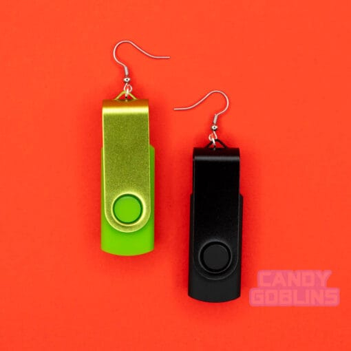 A pair of USB stick earrings, one USB is black, the other is a bright green. They are photographed against a red background.