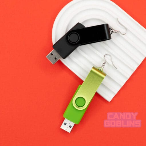 A pair of USB stick earrings, one USB is black, the other is a bright green. They are photographed against a white rainbow prop and a red background.