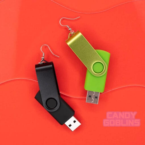 A pair of USB stick earrings, one USB is black, the other is a bright green. They are photographed against a red background.