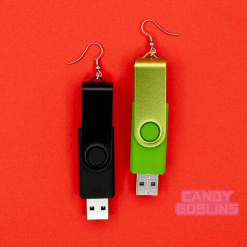 A pair of USB stick earrings, one USB is black, the other is a bright green. They are photographed against a red background.