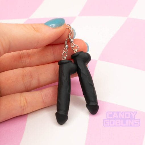 A pair of black dildo earrings being held by someone
