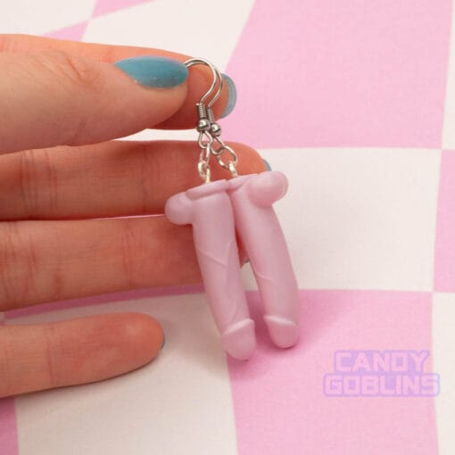 A pair of pink dildo earrings being held by someone