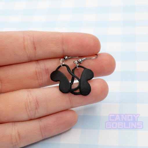 A pair of eye mask earrings being held by someone