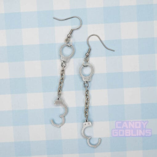 A pair of handcuff earrings, they have a metal chain connecting the cuffs