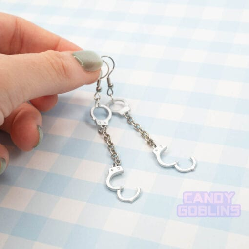 A pair of handcuff earrings, they have a metal chain connecting the cuffs