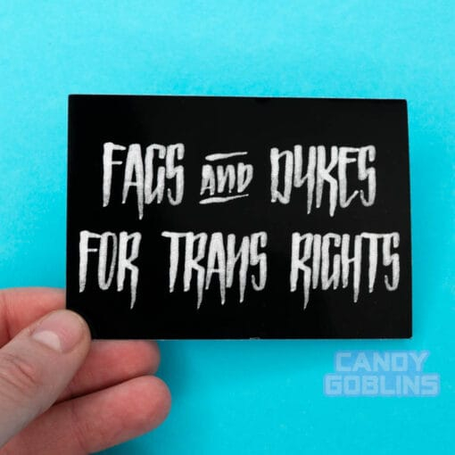 A person holds a Fags and Dykes for Trans Rights sticker against a cyan background