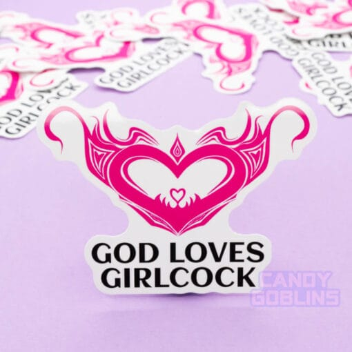 A sticker that reads "God Loves Girlcock" stands vertically. Behind, you can see more of the same sticker scattered around.